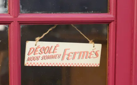 Panneau "Désolé, nous sommes fermés" sur une porte rouge. Il est donc probable que ce commerce ne soit pas ouvert le 1er mai.