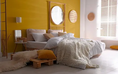 Une chambre d'adulte lumineuse avec un mur jaune soleil, un lit douillet et une décoration murale en rotin.