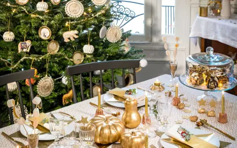 Déco table de Noël pas cher à faire soi-même : sapin décoré, citrouilles dorées, guirlandes lumineuses et vaisselle festive créent une ambiance chaleureuse.