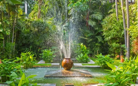 Fontaine d'eau jaillissant d'un pot en terre cuite, au cœur d'un jardin luxuriant. Une **original déco jardin récupération** qui invite à la détente.