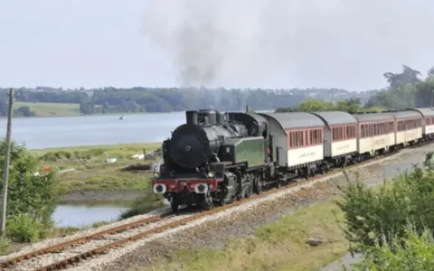 Le petit train du Trieux, avec ses tarifs attractifs, traverse un paysage verdoyant longeant une étendue d'eau.