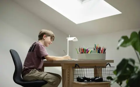 Un jeune garçon dessine joyeusement à son bureau sous pente, éclairé par une grande fenêtre de toit.