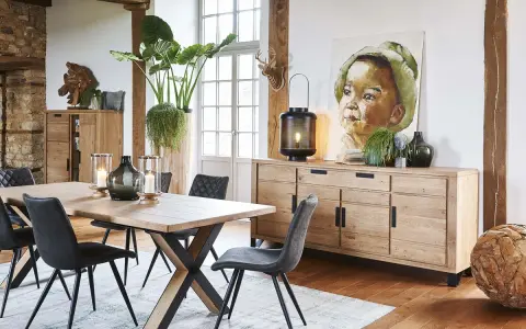 Salle à manger style industriel avec table en bois, chaises grises, buffet en chêne et tableau d'enfant.