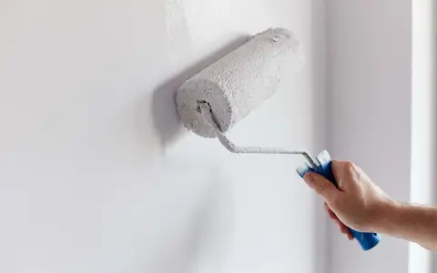 Main tenant en main un rouleau, il commence à peindre un mur d'une couleur blanche éclatante.