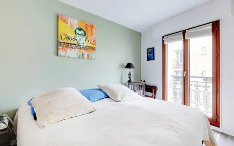 Chambre avec un mur vert pastel, un lit blanc et une œuvre d'art de Woody Allen. On dirait qu'ils ont décidé de peindre 2 murs sur 4.