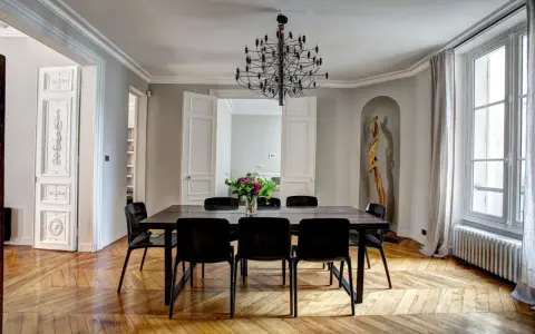 Salle à manger élégante dans un type de maison haussmannien, avec parquet ancien, lustre moderne et bouquet de fleurs.
