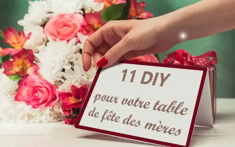 Une main dépose une carte "11 DIY pour votre table de fête des mères" près d'un bouquet de fleurs roses et blanches.