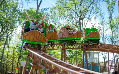 Famille joyeuse sur des wagons de montagnes russes en bois dans un parc attraction ile de france.