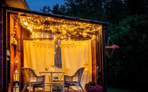 Une terrasse accueillante illuminée par des guirlandes lumineuses, une belle idée éclairage terrasse pour des soirées magiques. Meubles en rotin et fleurs ajoutent à l'ambiance.