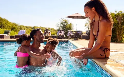 Famille s'amusant dans une piscine, un père avec ses deux filles, une mère assise au bord. Le cadre parfait pour le meilleur center parc France.