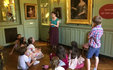 Visite guidée d'un musée dans les Yvelines : des enfants écoutent attentivement une guide devant des tableaux.