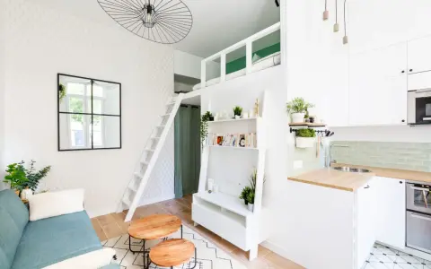 Aménagement intérieur appartement optimisé avec mezzanine, canapé bleu, étagères et coin cuisine moderne.
