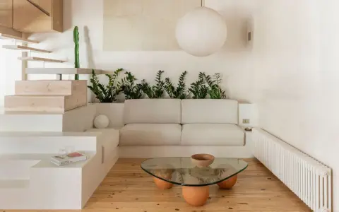 Salon au style wabi sabi, avec un canapé blanc, une table basse en verre et bois, des plantes vertes et un escalier en bois brut.