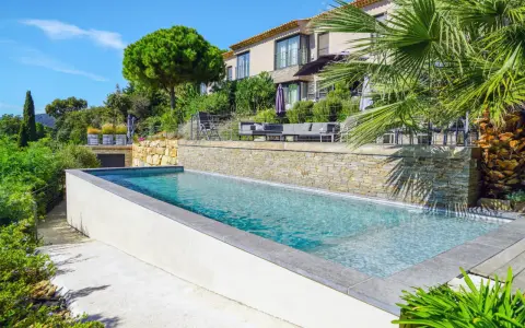 Magnifique piscine semi enterrée avec habillage en pierre, bordée par une terrasse et un jardin luxuriant, devant une villa moderne.
