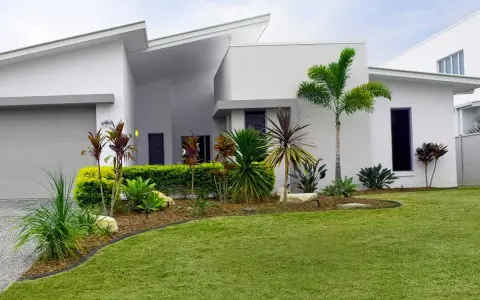Parterre luxuriant devant une maison moderne aux lignes épurées, avec des palmiers et des plantes tropicales.
