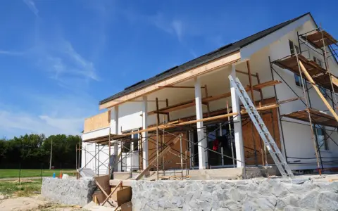 Chantier d'une maison en cours de rénovation, avec échafaudages et une échelle. Projet d'agrandissement de maison en vue.