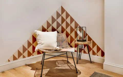 Un coin cosy avec un fauteuil en rotin, un coussin blanc et un motif géométrique sur le mur. Une belle idée motif peinture mur pour un style unique.