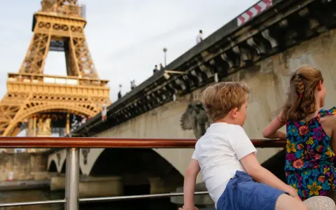 Deux enfants profitent d'une croisière sur la Seine à Paris la nuit, avec la Tour Eiffel illuminée en arrière-plan.