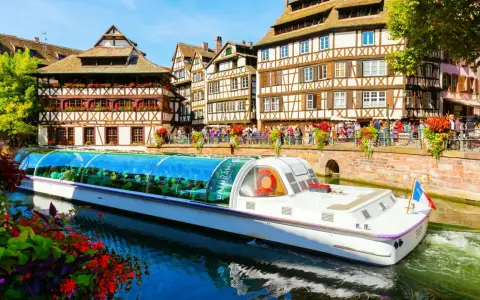 Bateau touristique naviguant sur un canal à la Petite France à Strasbourg, avec ses maisons à colombages et ses balcons fleuris.
