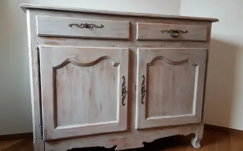 Buffet ancien patiné, avec deux tiroirs et deux portes ornées de poignées en bronze. Le bois présente une finition usée pour un style vintage.