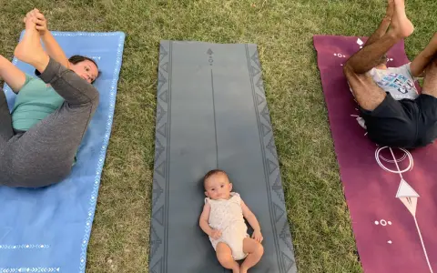 Un bébé sur un tapis de yoga, entouré de ses parents pratiquant le yoga. Une séance de yoga pour enfants en plein air.