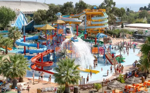 Vaste parc aquatique dans le sud de la France, avec de nombreux toboggans colorés, des jeux d'eau et des palmiers. Ambiance festive et familiale.