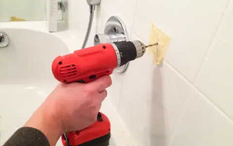 Main tenant utilise une perceuse pour percer du carrelage mural dans une salle de bain.