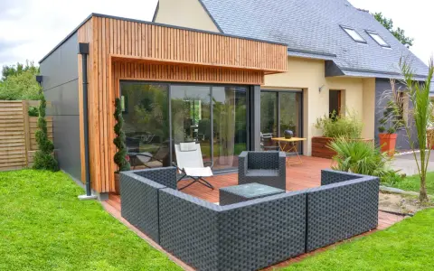 Agrandissement maison ossature bois avec terrasse moderne et mobilier extérieur.