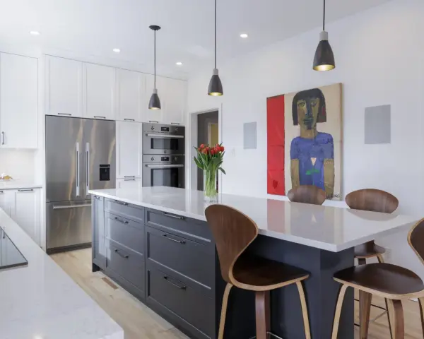 Cuisine moderne avec îlot central gris, comptoirs en quartz, armoires blanches et tableau abstrait. Idées pour comment rénover sa cuisine.