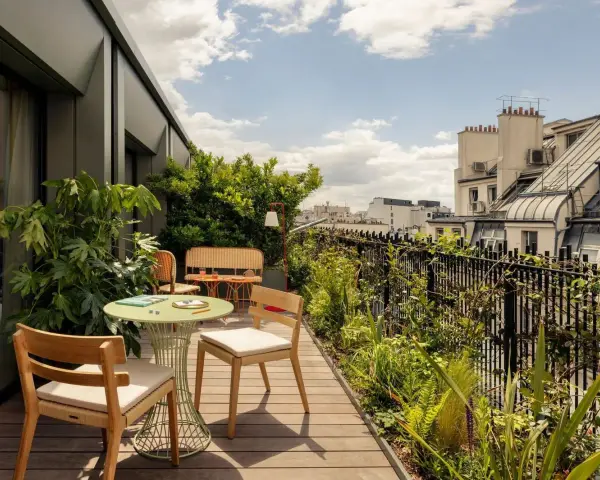 Aménagement balcon 10m2 : table ronde verte, chaises en bois, banquette en rotin, plantes luxuriantes et vue sur les toits de Paris.