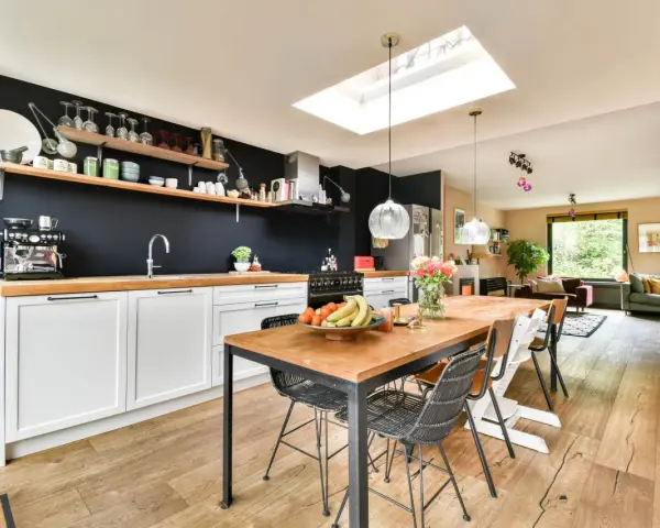 Cuisine moderne avec îlot central, parfait pour rénover vieille cuisine. Table en bois, chaises design, et mur noir avec étagères.