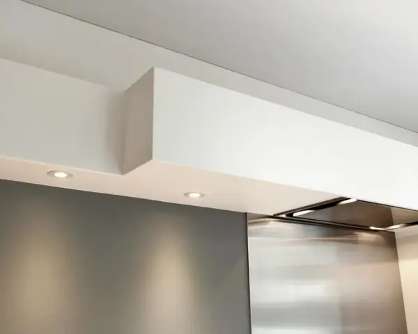 Éclairage discret sous un faux plafond de cuisine moderne, intégrant une hotte aspirante en inox.