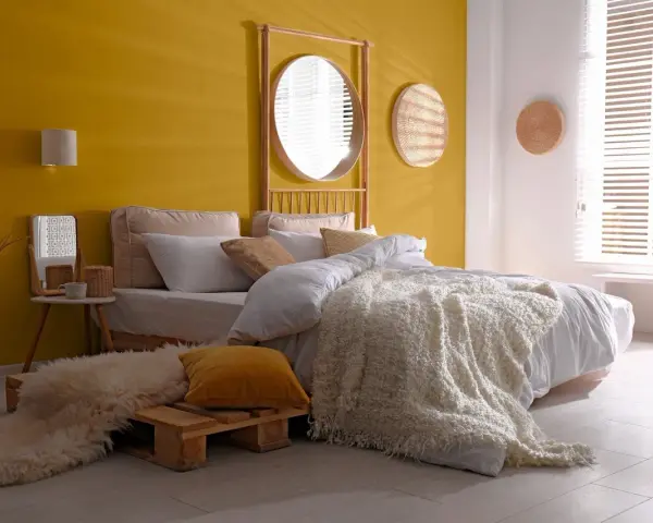 Une chambre d'adulte lumineuse avec un mur jaune soleil, un lit douillet et une décoration murale en rotin.