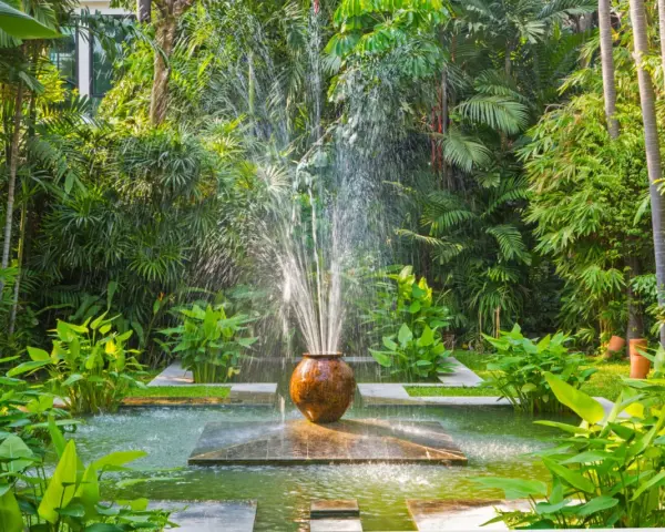 Fontaine d'eau jaillissant d'un pot en terre cuite, au cœur d'un jardin luxuriant. Une **original déco jardin récupération** qui invite à la détente.