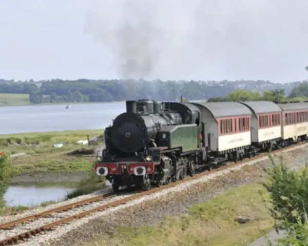 Le petit train du Trieux, avec ses tarifs attractifs, traverse un paysage verdoyant longeant une étendue d'eau.