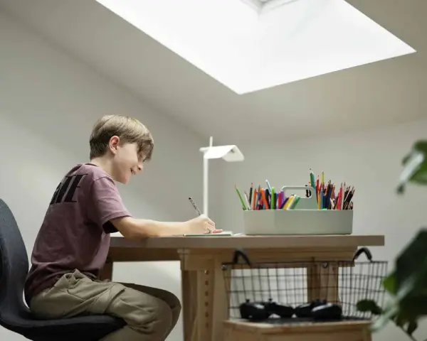 Un jeune garçon dessine joyeusement à son bureau sous pente, éclairé par une grande fenêtre de toit.