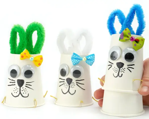 Trois adorables lapins de Pâques bricolage faits avec des gobelets en papier, des pompons et des yeux mobiles. Parfait pour une activité de Pâques !