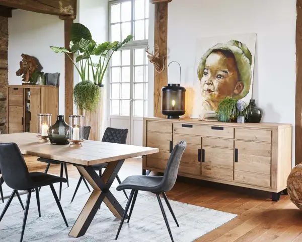 Salle à manger style industriel avec table en bois, chaises grises, buffet en chêne et tableau d'enfant.