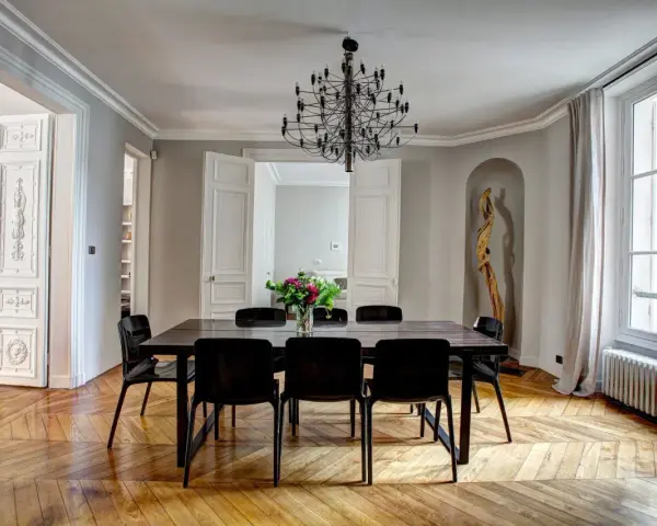 Salle à manger élégante dans un type de maison haussmannien, avec parquet ancien, lustre moderne et bouquet de fleurs.
