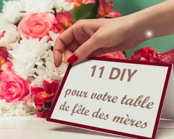 Une main dépose une carte "11 DIY pour votre table de fête des mères" près d'un bouquet de fleurs roses et blanches.