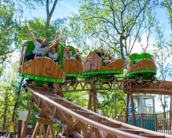 Famille joyeuse sur des wagons de montagnes russes en bois dans un parc attraction ile de france.