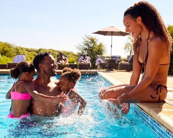 Famille s'amusant dans une piscine, un père avec ses deux filles, une mère assise au bord. Le cadre parfait pour le meilleur center parc France.