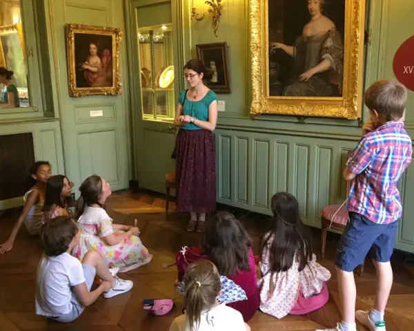 Visite guidée d'un musée dans les Yvelines : des enfants écoutent attentivement une guide devant des tableaux.