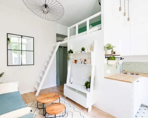Aménagement intérieur appartement optimisé avec mezzanine, canapé bleu, étagères et coin cuisine moderne.