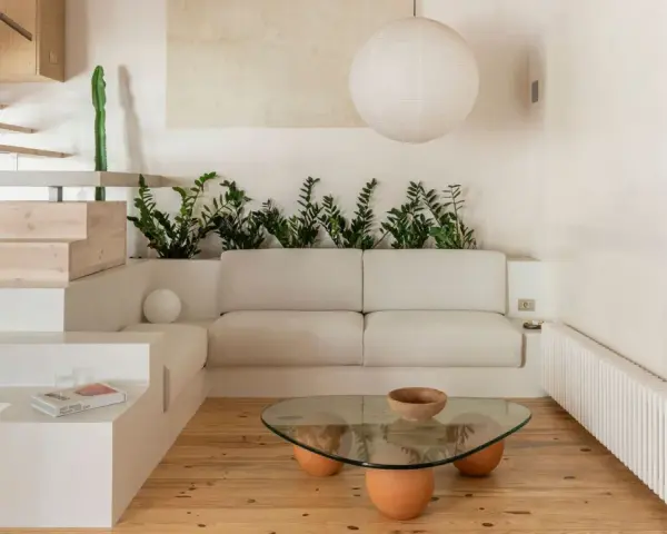 Salon au style wabi sabi, avec un canapé blanc, une table basse en verre et bois, des plantes vertes et un escalier en bois brut.