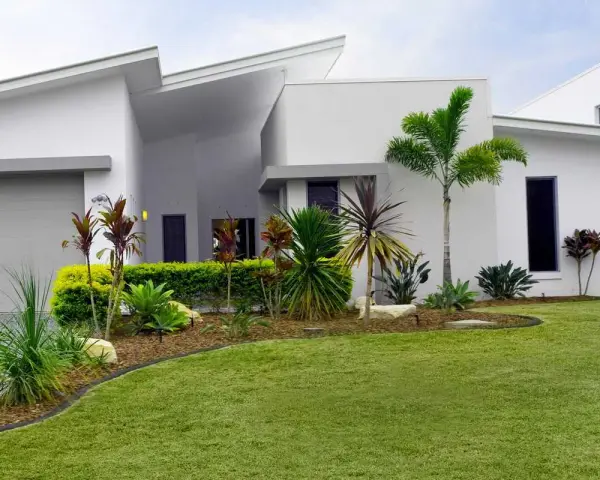 Parterre luxuriant devant une maison moderne aux lignes épurées, avec des palmiers et des plantes tropicales.