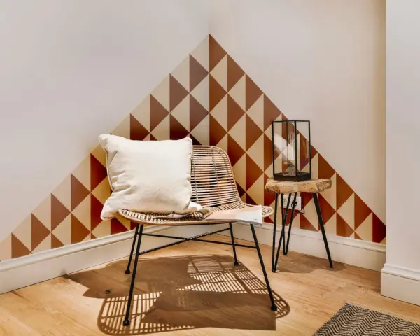 Un coin cosy avec un fauteuil en rotin, un coussin blanc et un motif géométrique sur le mur. Une belle idée motif peinture mur pour un style unique.