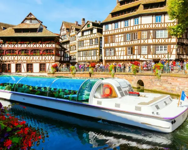 Bateau touristique naviguant sur un canal à la Petite France à Strasbourg, avec ses maisons à colombages et ses balcons fleuris.