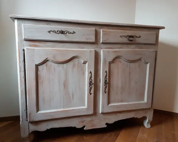 Buffet ancien patiné, avec deux tiroirs et deux portes ornées de poignées en bronze. Le bois présente une finition usée pour un style vintage.