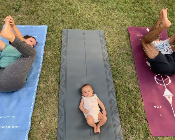 Un bébé sur un tapis de yoga, entouré de ses parents pratiquant le yoga. Une séance de yoga pour enfants en plein air.